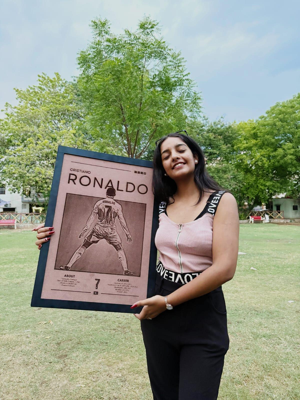 Woman holding a framed picture of a sports player on a grassy field with trees in the background